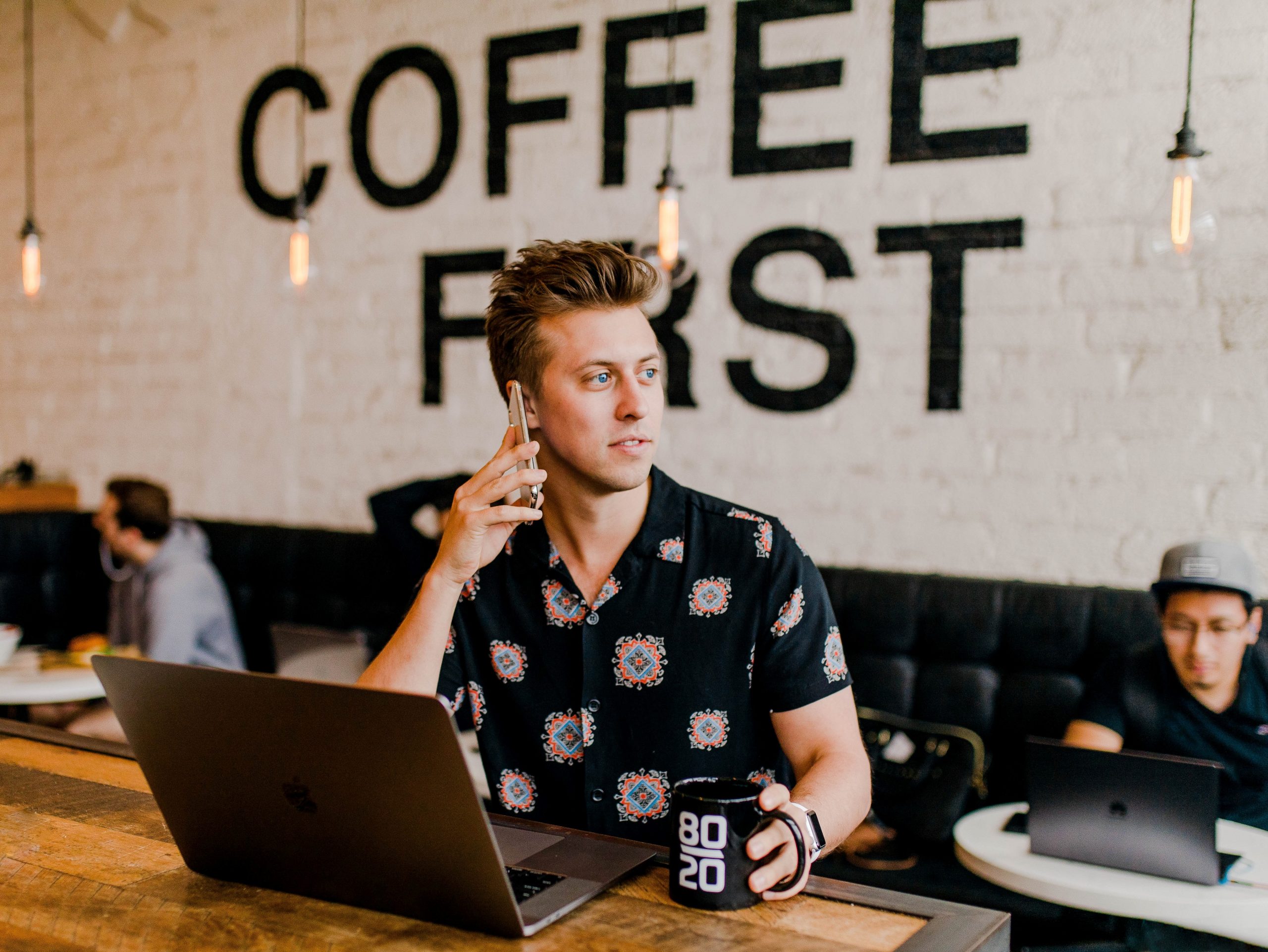 Junger Mann im Coffeeshop vor dem Computer beim Telefonieren